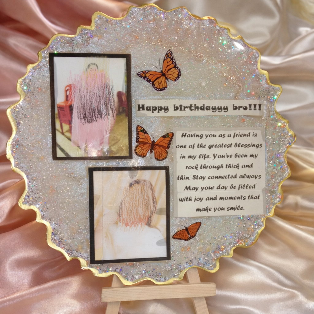 A glittery round resin photo frame plaque with gold edges, featuring printed photos, birthday message text, and butterfly decorations, displayed on a small wooden stand against a satin fabric background. Handmade Custom vs Ready Resin Pieces: A Complete Comparison