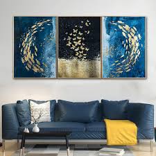 Three-panel abstract wall art with blue and gold butterfly patterns displayed above a modern blue sofa in a living room setting.a sofa — resin art festive décor.
